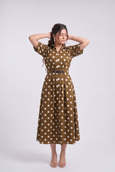 A woman modeling a brown short-sleeve midi dress with white polka dots and a matching belt, standing against a light gray studio background.