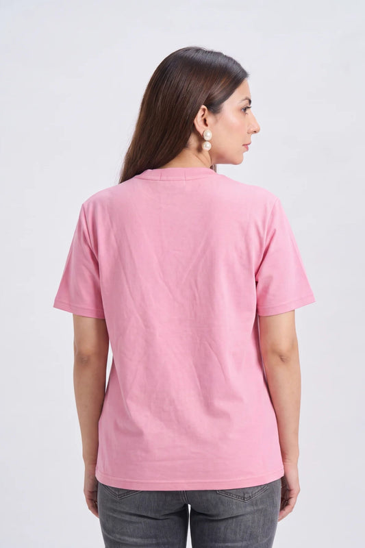 A woman viewed from the back wearing a light pink short-sleeve crewneck t-shirt and dark gray jeans, standing against a plain light gray studio background.