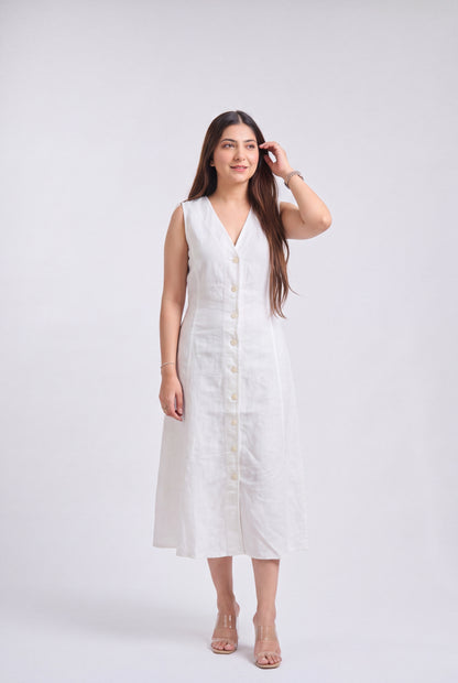 A woman modeling a sleeveless white linen midi dress with a V-neckline and a row of cream buttons down the front, standing against a light gray studio background.