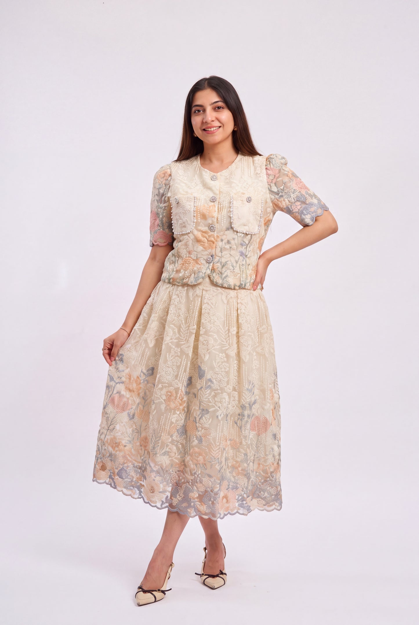 A woman modeling a cream-colored floral printed dress with a structured vest and short puff sleeves, standing against a plain light gray studio background.