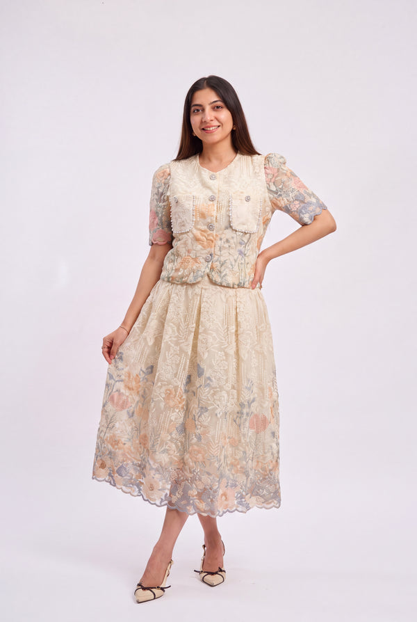 A woman modeling a cream-colored floral printed dress with a structured vest and short puff sleeves, standing against a plain light gray studio background.