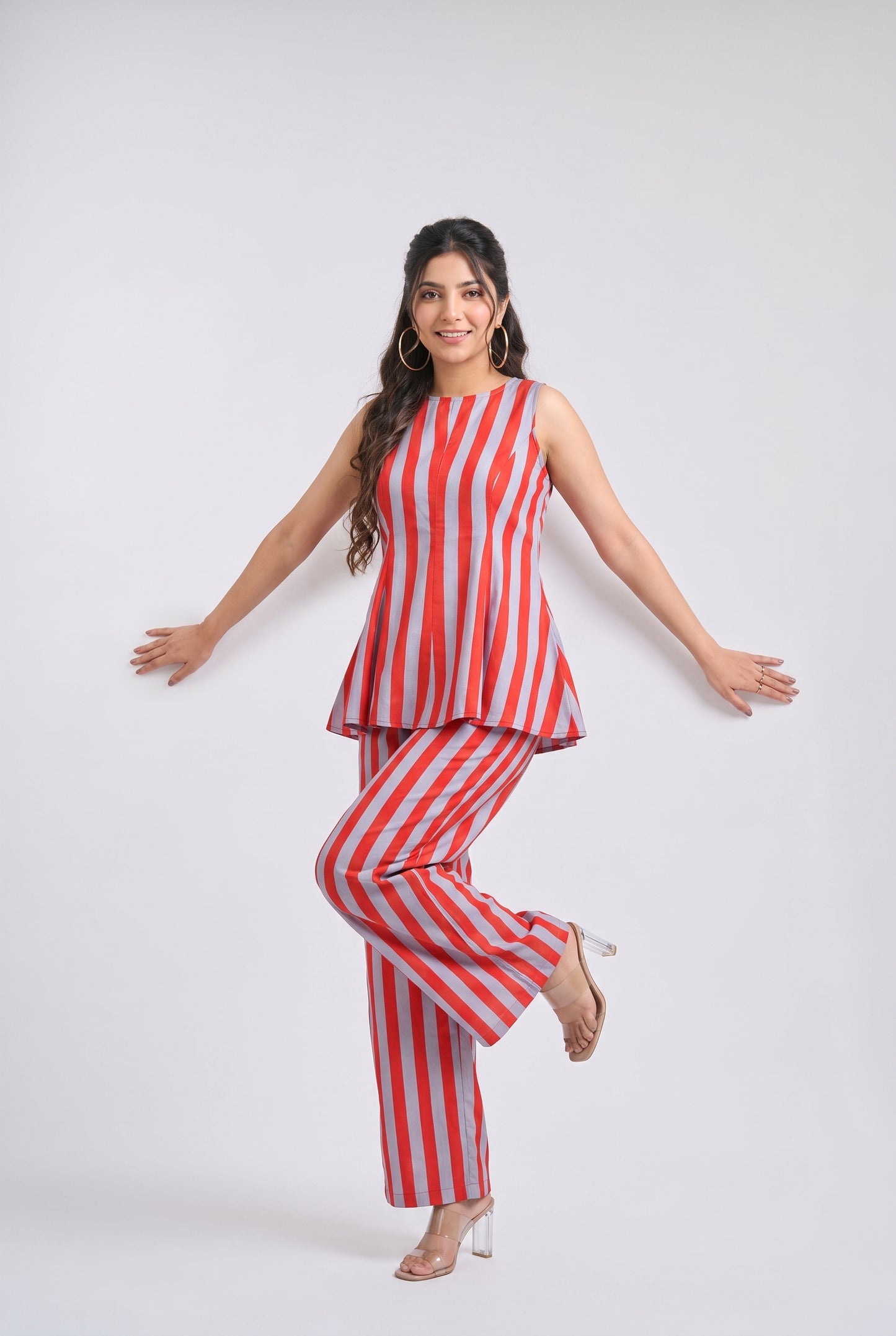 A woman modeling a sleeveless red and white vertically striped peplum top and matching wide-leg pants against a light gray studio background.