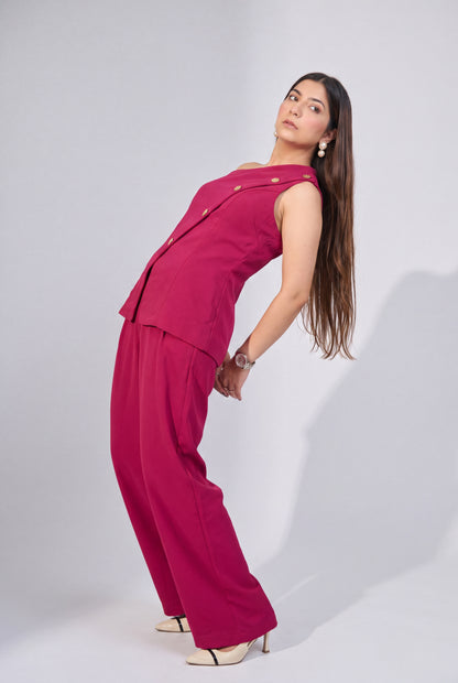 A woman modeling a bright magenta two-piece outfit consisting of a sleeveless button-front vest and matching wide-leg pants, posed against a light gray studio background.