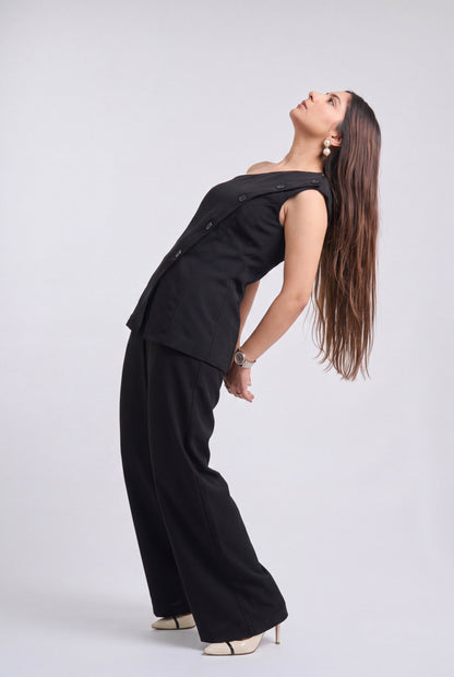 A woman modeling a black sleeveless vest and matching wide-leg trousers, posing in a studio setting against a light gray background.
