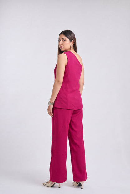 A woman modeling a bright magenta two-piece set consisting of a sleeveless top and wide-leg trousers, shown from a side-back angle against a light gray studio background.