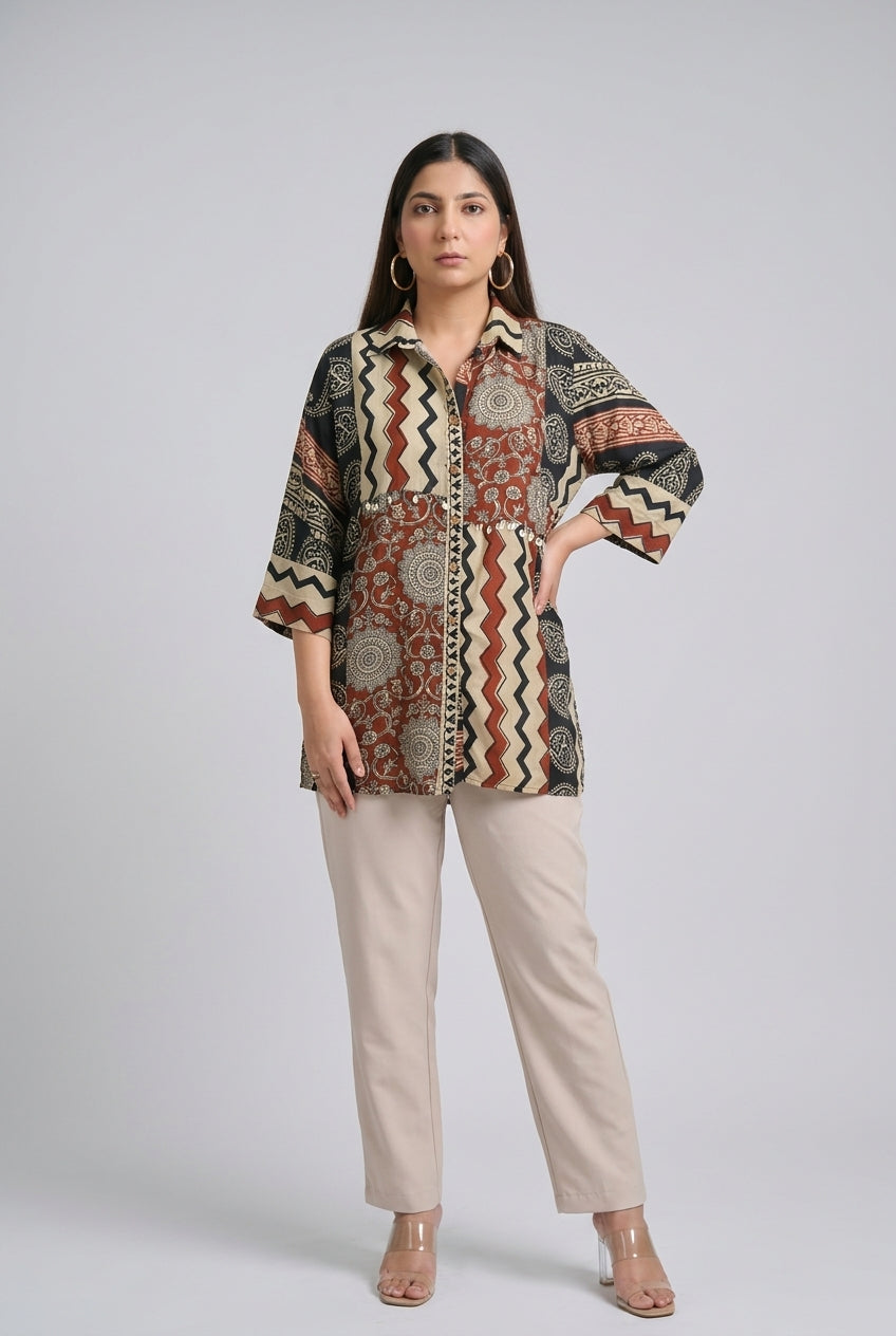 A woman modeling a patterned button-up shirt with beige straight-leg pants and clear high-heeled sandals, standing against a light gray studio background.