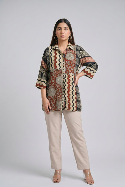 A woman modeling a patterned button-up shirt with beige straight-leg pants and clear high-heeled sandals, standing against a light gray studio background.