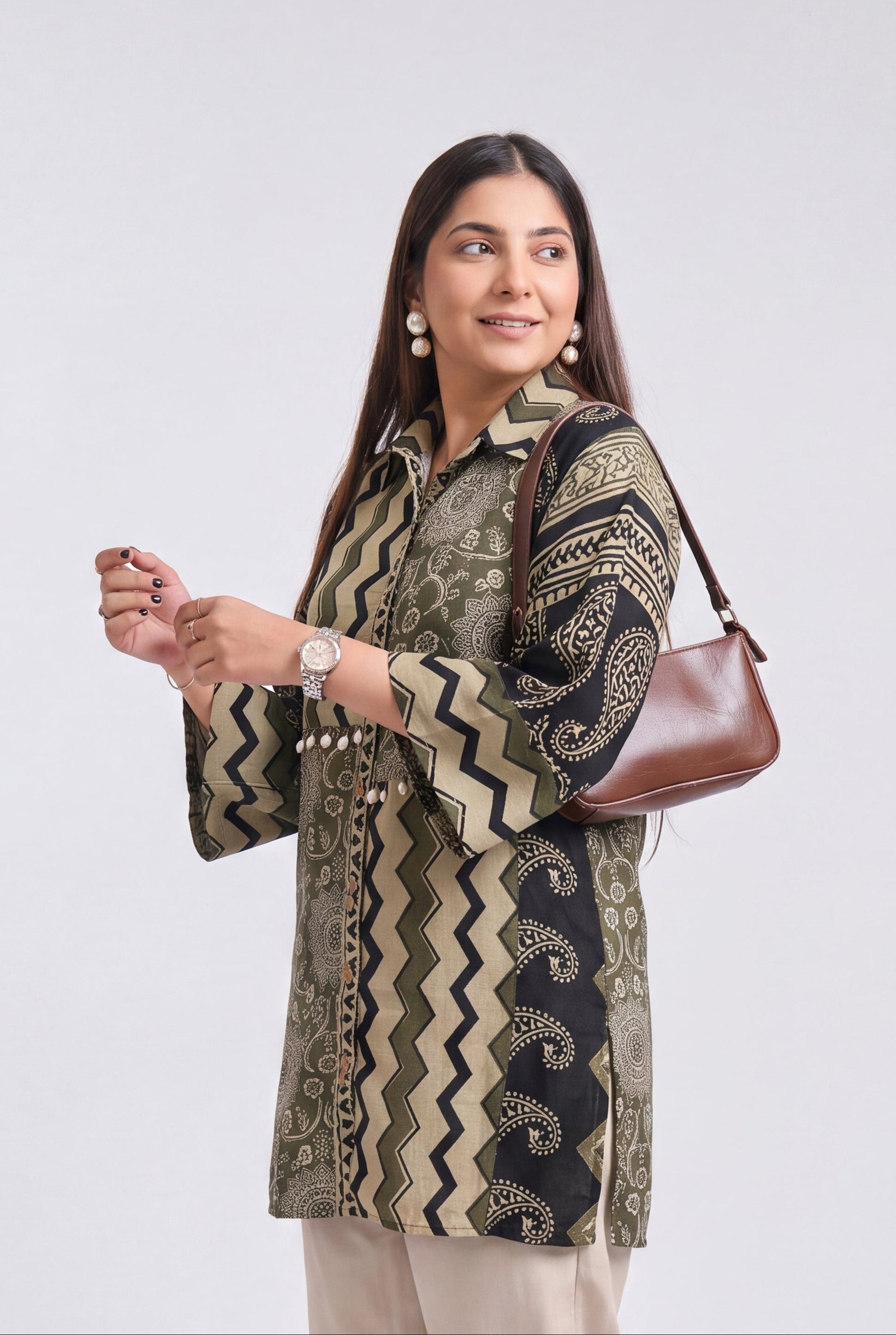 A woman modeling a patterned kurta with beige straight-leg pants, a brown shoulder bag, and clear high-heeled sandals, photographed against a light gray studio background.