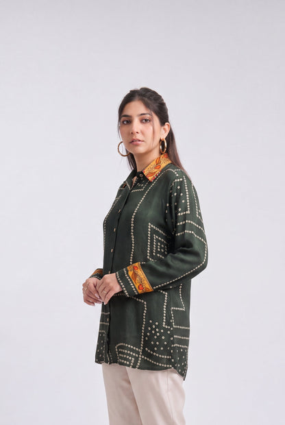 A woman modeling a dark green printed kurta with orange and white geometric patterns, paired with beige trousers and clear high-heeled sandals, against a light gray studio background.