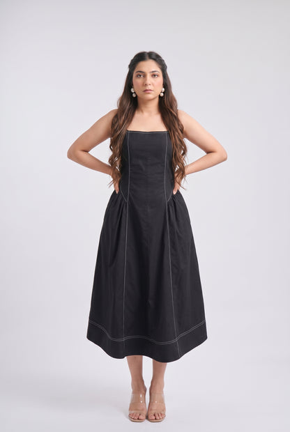 A woman modeling a black strapless midi dress with structured shoulders and a flared skirt, standing against a light gray studio background.