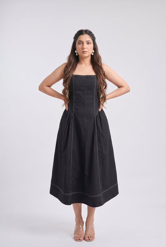 A woman modeling a black strapless midi dress with structured shoulders and a flared skirt, standing against a light gray studio background.