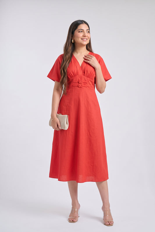 A woman modeling a bright Red midi dress with short sleeves, a V-neckline, and a matching fabric belt with two gold-tone buttons, set against a plain light gray studio background.