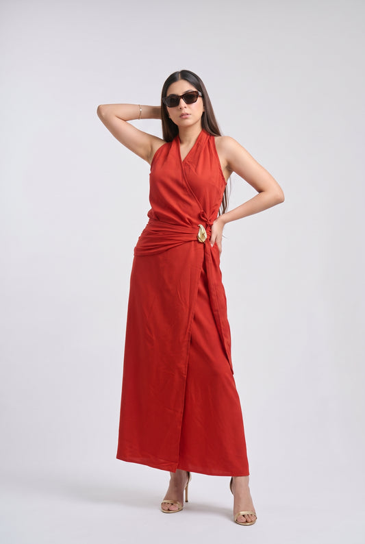 A woman modeling a sleeveless red wrap-style maxi dress with a halter neckline and a draped tie detail at the waist, posed against a light gray studio background.