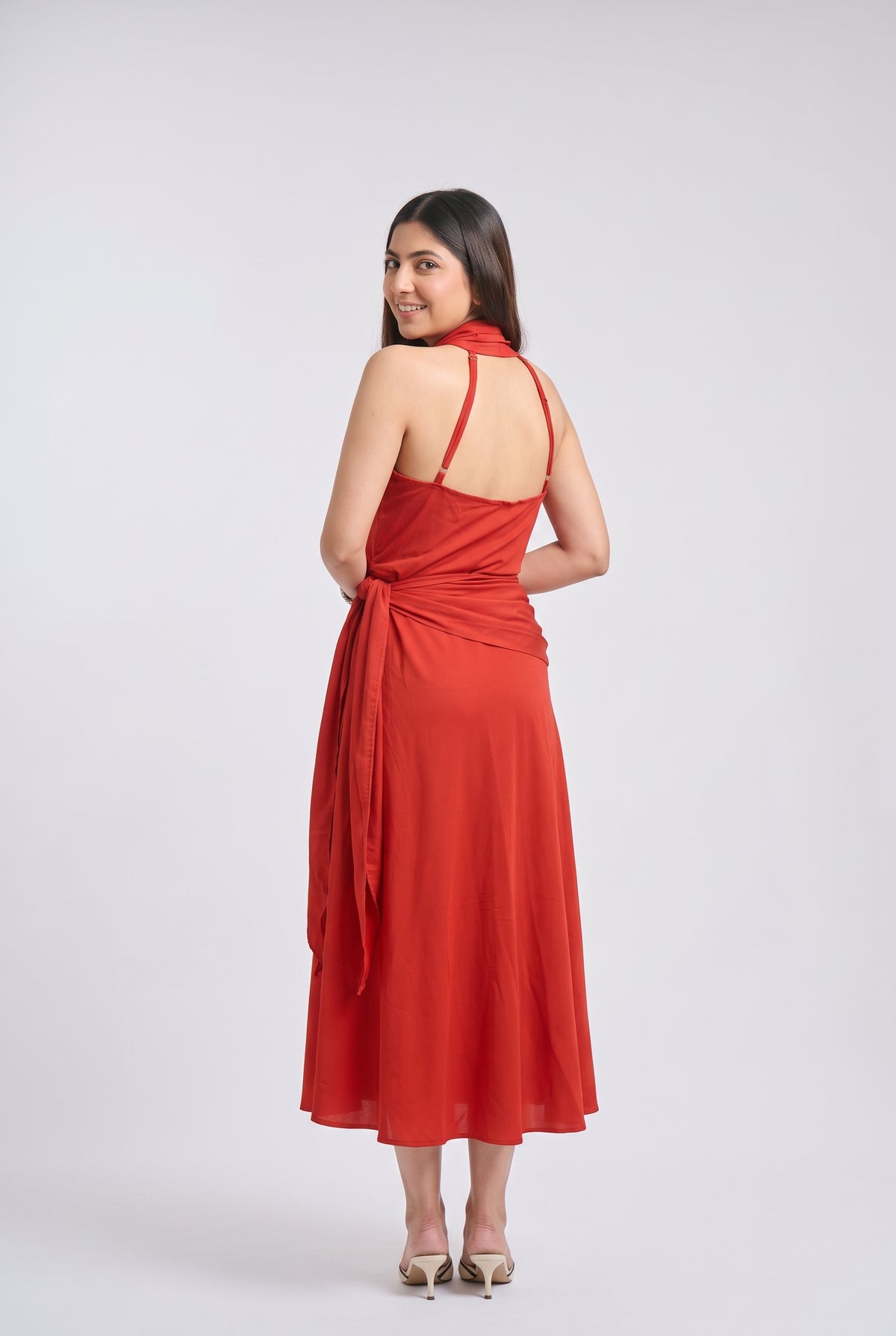 A woman modeling a red halter-neck midi dress, shown from the back against a light gray studio background.
