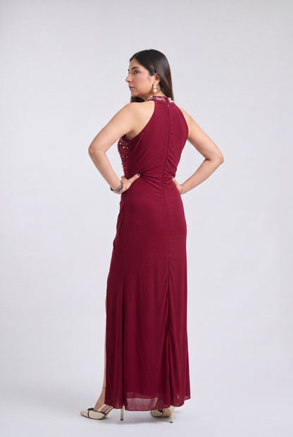 A woman modeling a sleeveless, floor-length burgundy maxi dress from the back, standing against a light gray studio background.