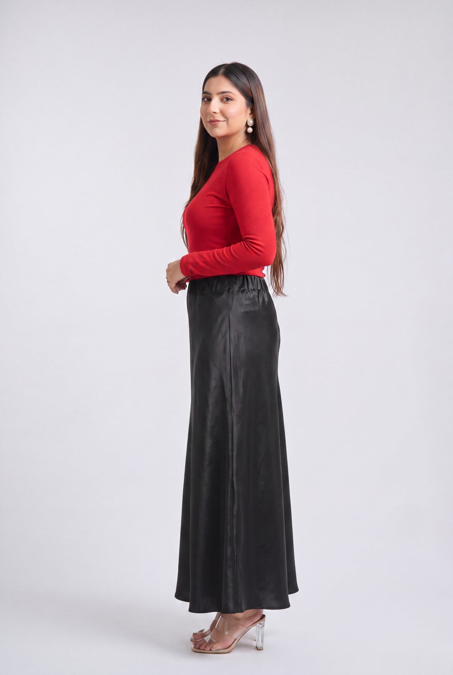 A woman modeling a long-sleeve red top and a high-waisted black satin maxi skirt against a light gray studio background.