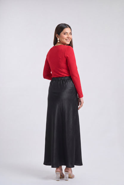 A woman is shown from the back wearing a bright red long-sleeve top and a long black skirt, standing against a light gray studio background.