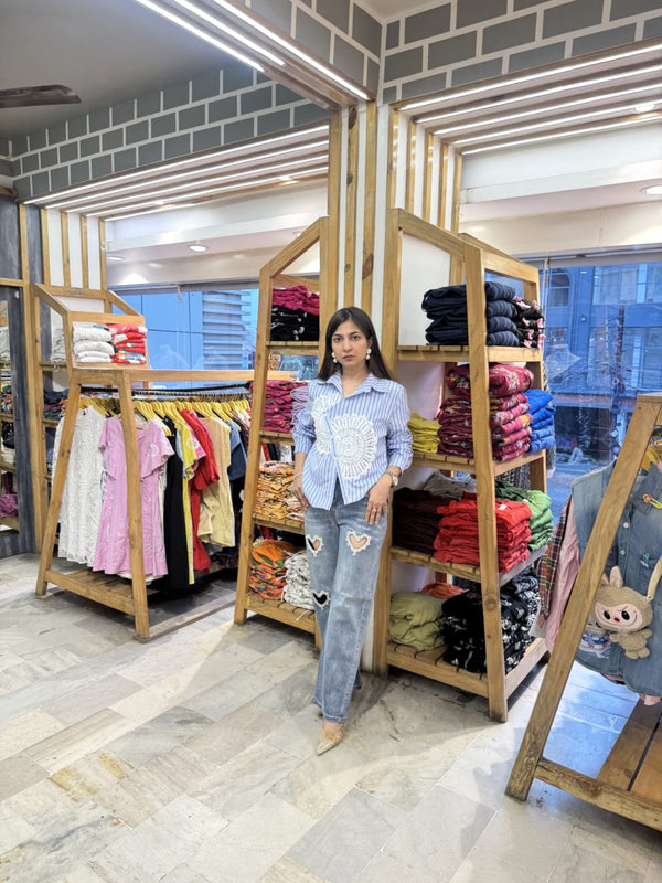 Woman standing in a clothing store with racks of clothes and a brick wall.