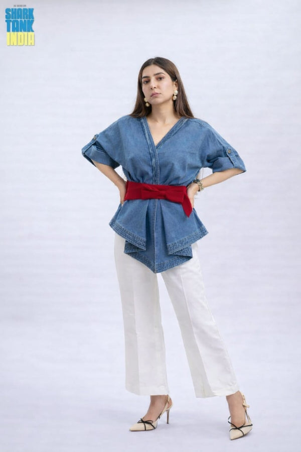 Woman wearing a blue denim top with a red belt and white pants on a white background