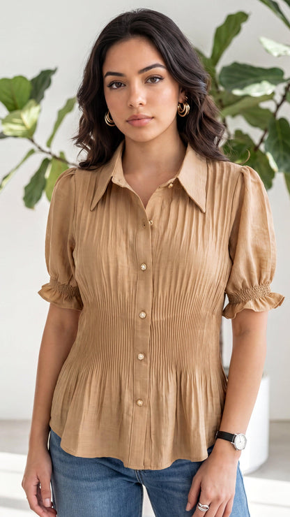 Woman wearing a beige blouse with puffed sleeves against a white wall with green leaves.