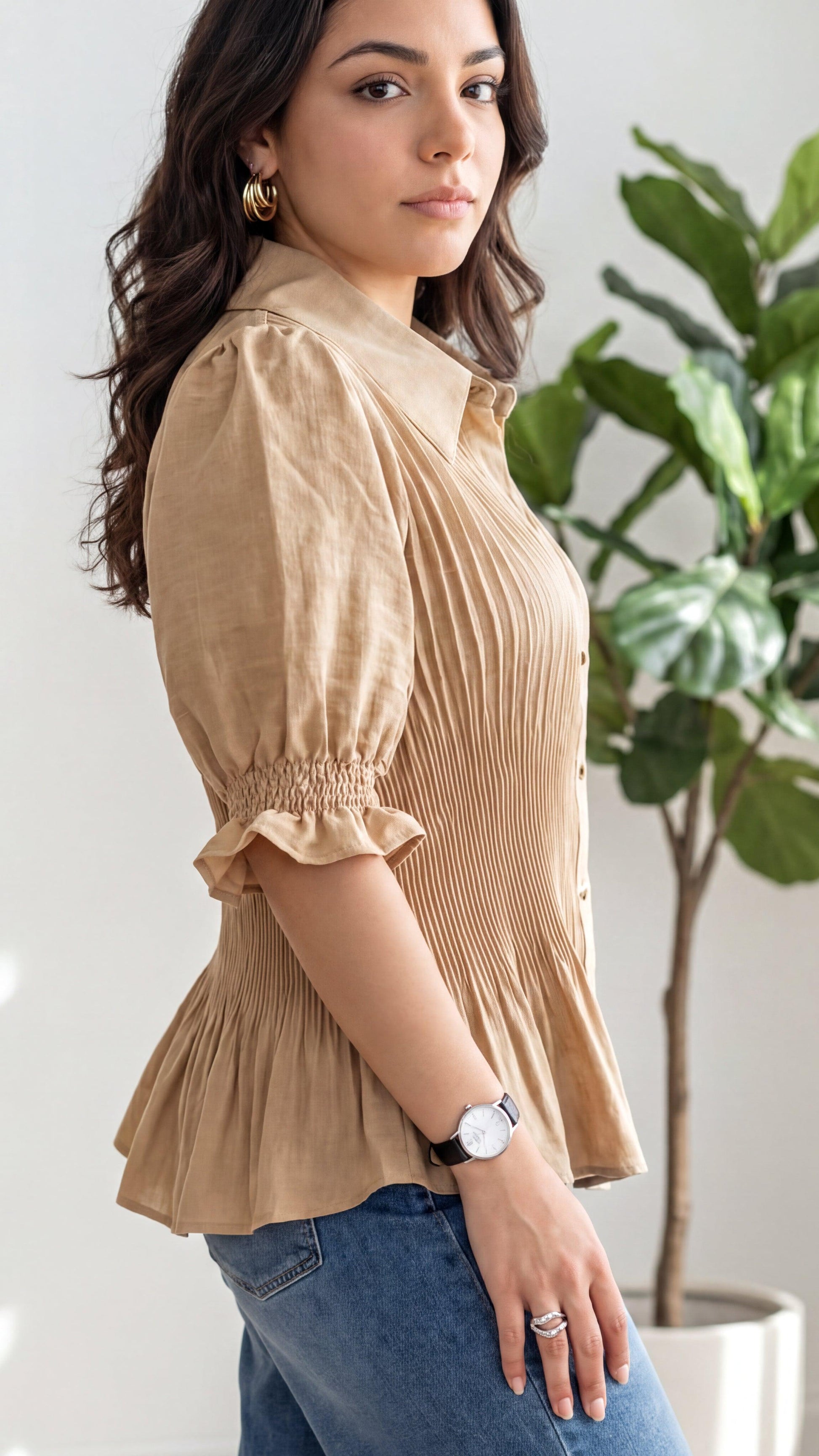 Woman wearing a beige blouse and blue jeans with a plant in the background