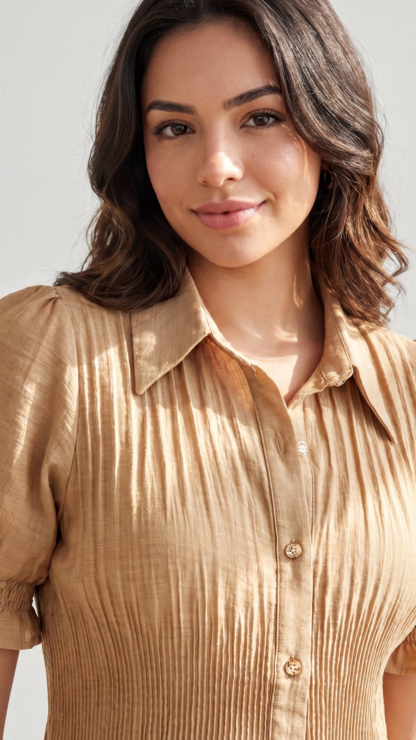 Woman wearing a beige button-up shirt against a plain background