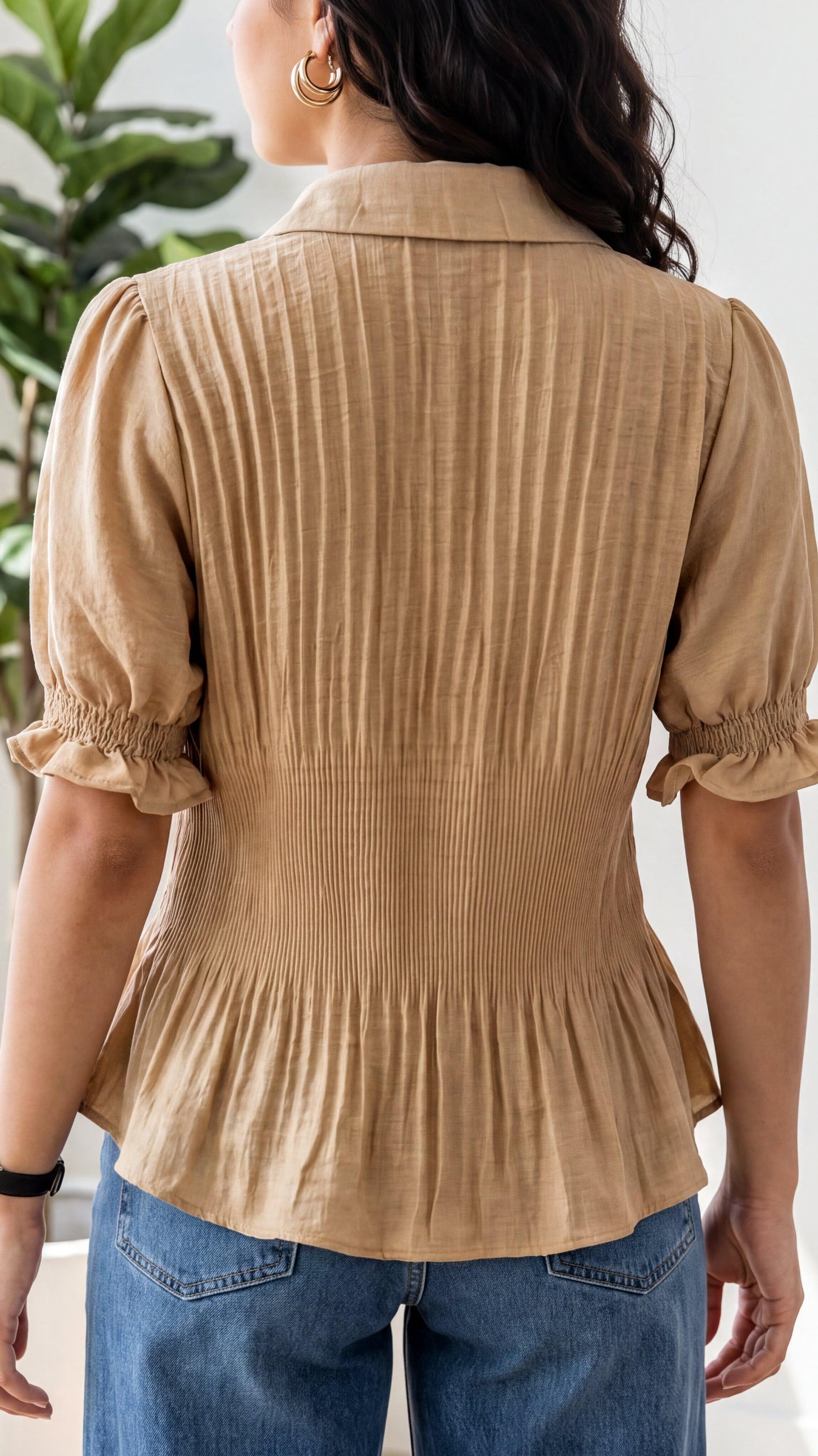 Person wearing a beige ribbed blouse with blue jeans, standing indoors.
