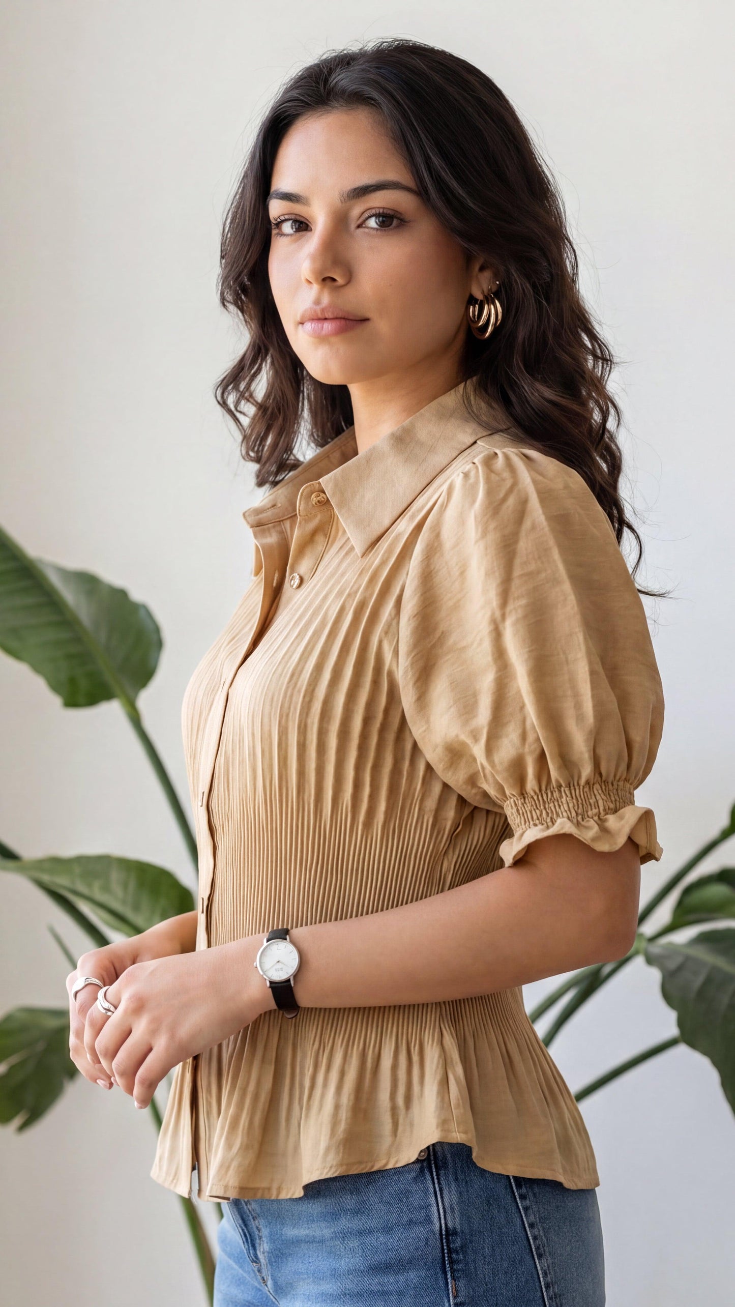 Woman wearing a beige blouse and blue jeans with a plant in the background