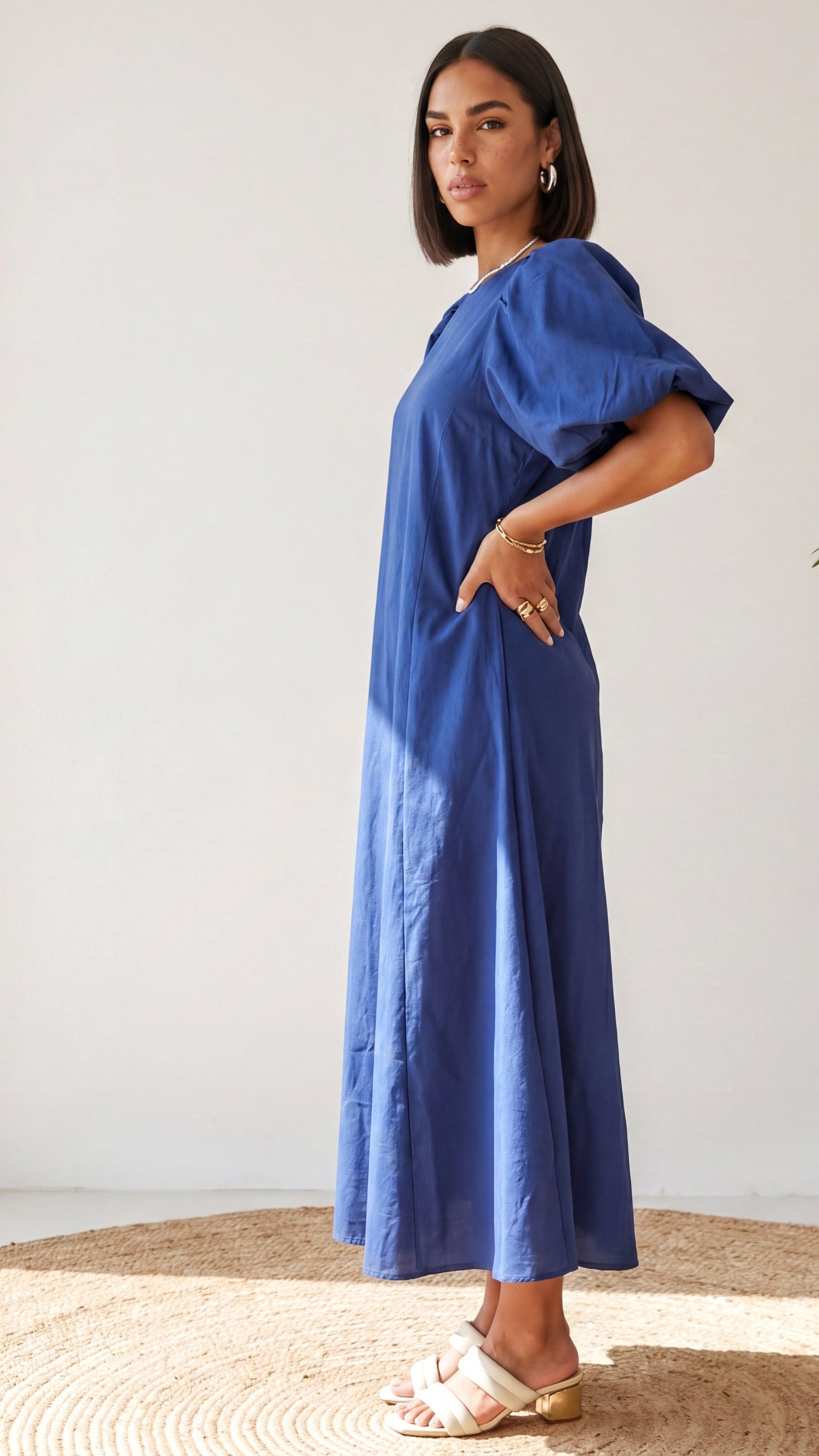 Woman wearing a blue dress standing on a textured surface with a white background