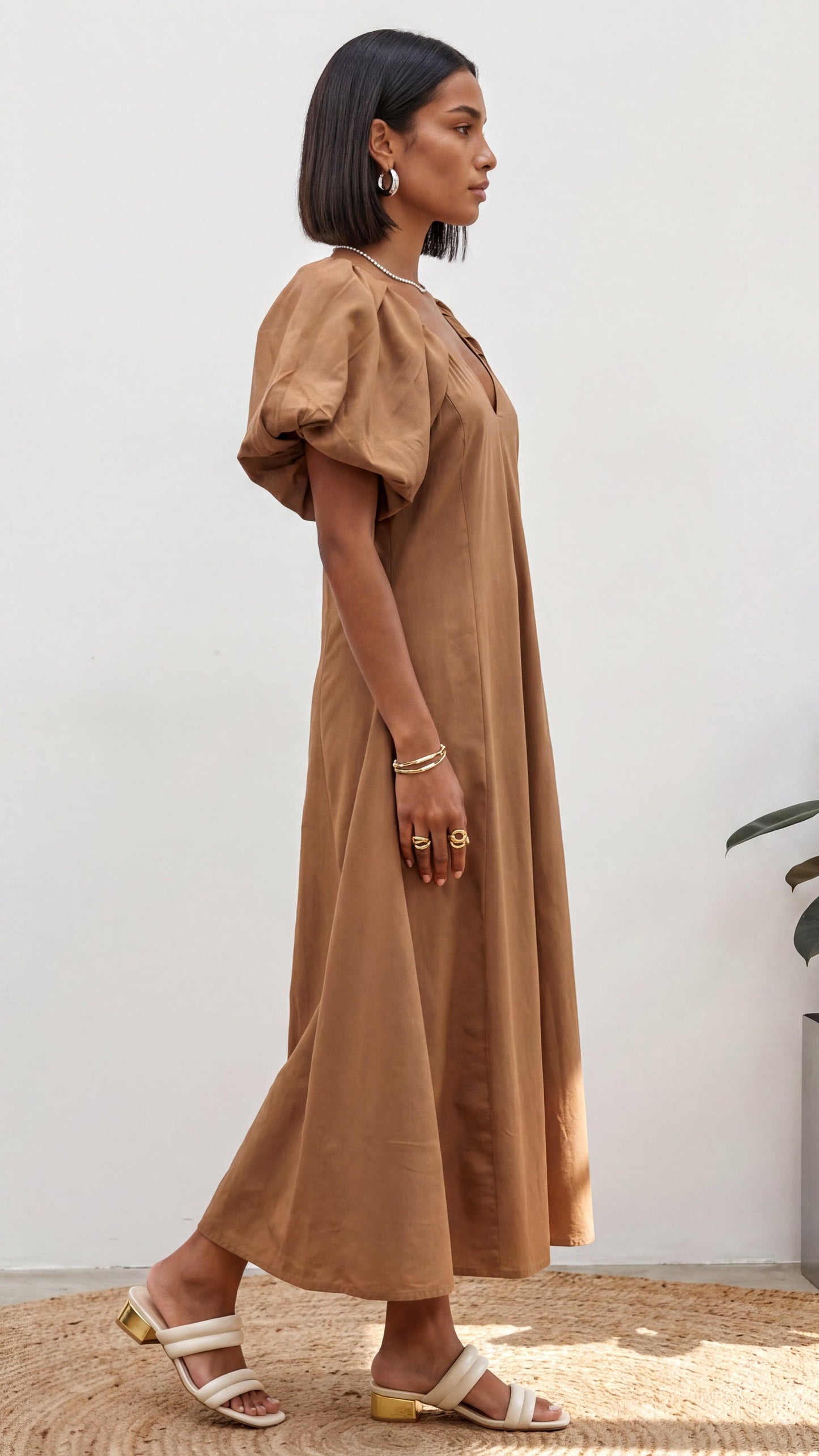 Woman wearing a brown dress standing against a white wall.
