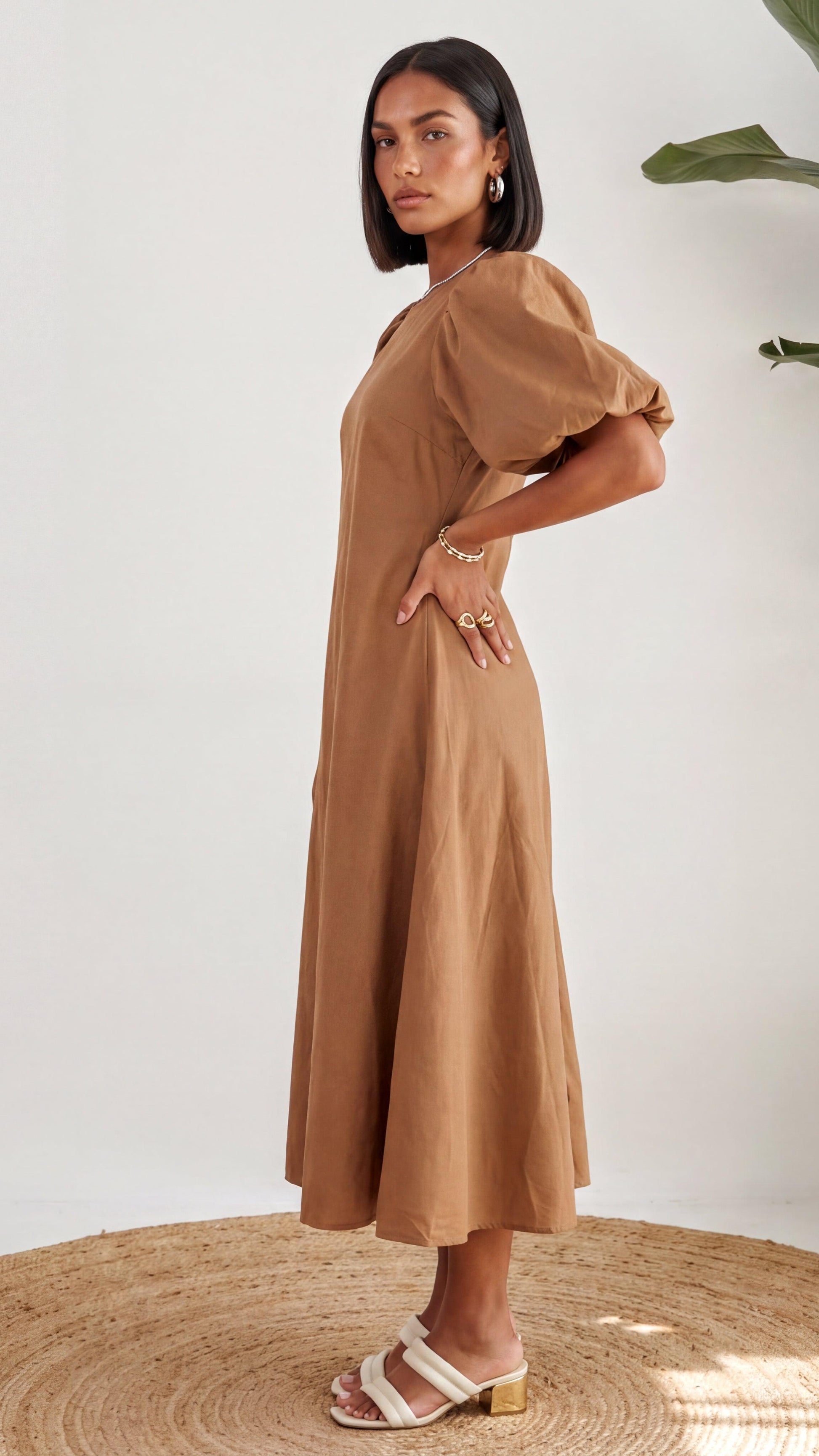 Woman wearing a brown dress standing on a woven mat with a white background