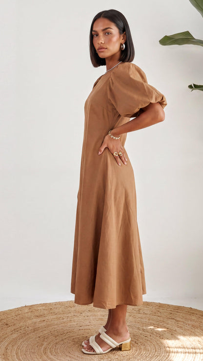 Woman wearing a brown dress standing on a woven mat with a white background