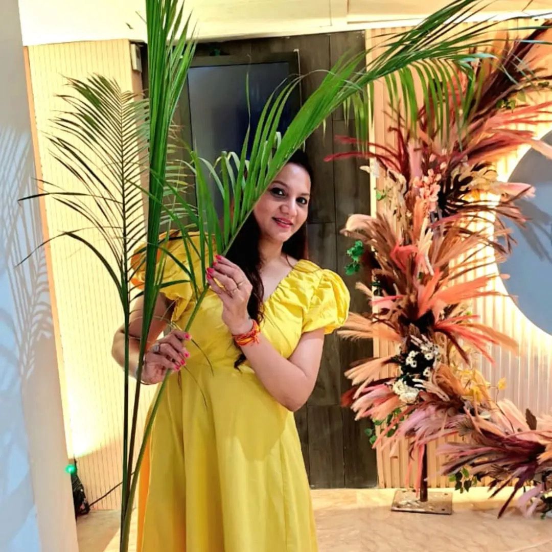 Woman in a yellow dress holding a plant with decorative elements in the background