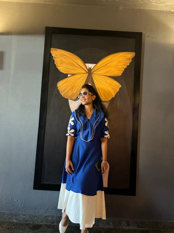 Woman in a blue dress standing next to a large framed picture of a yellow butterfly.