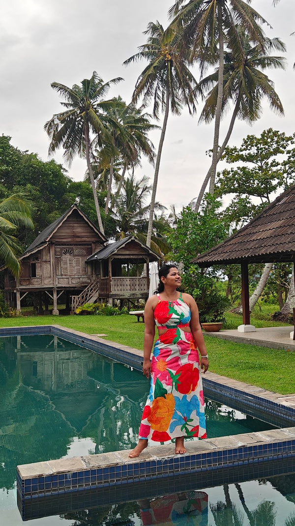Woman in a colorful dress standing by a pool with palm trees and wooden huts in the background