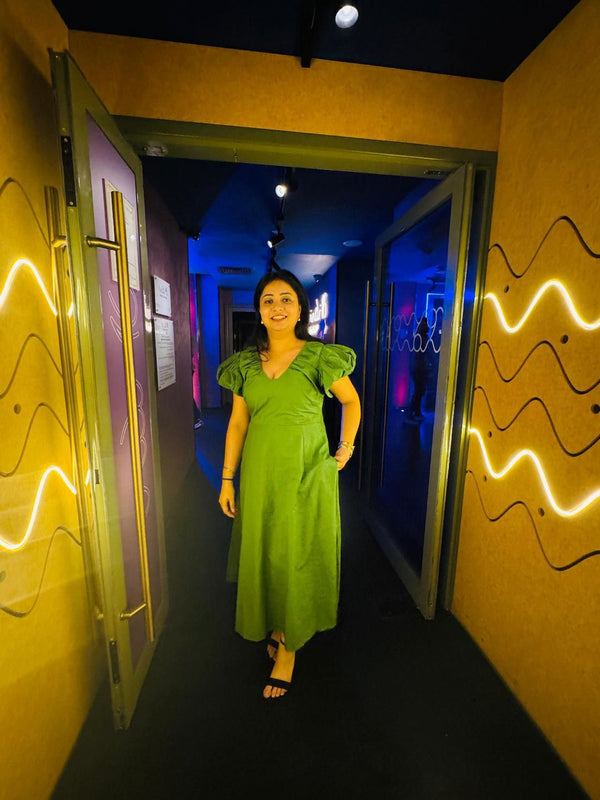 Woman in a green dress standing in a colorful hallway with wavy patterns on the walls.