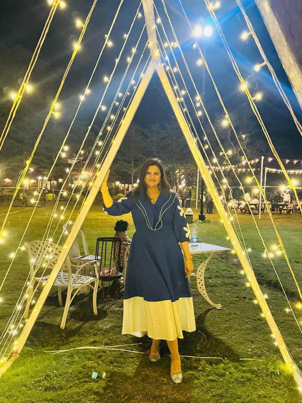 Woman in a blue dress standing under a string of lights at night.