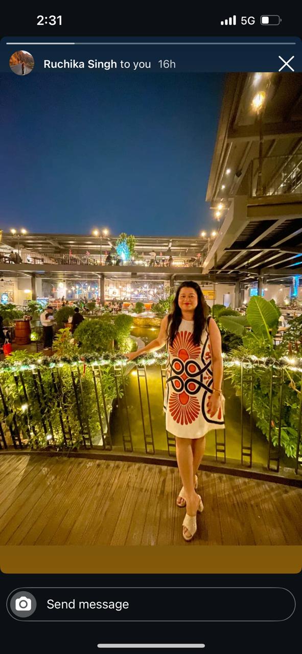 Woman in a colorful dress standing on a rooftop at night with lights and people in the background