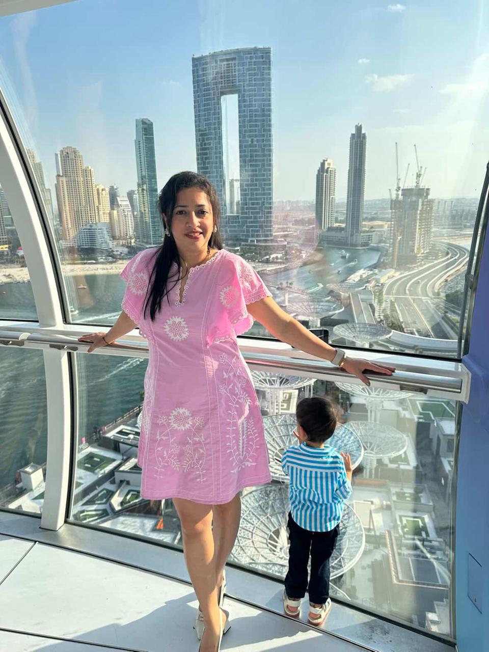 Woman in a pink dress with a child in a blue striped shirt standing in front of a city skyline view.