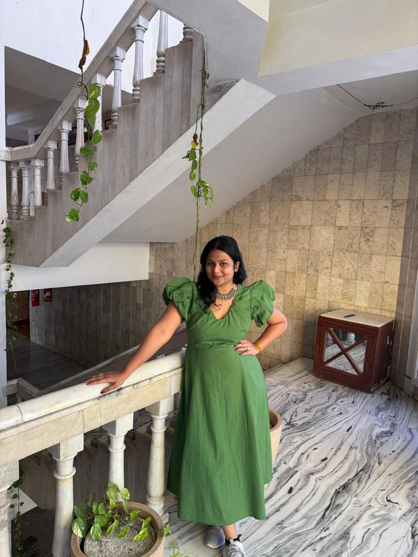 Woman in a green dress standing on a staircase with plants and a marble floor.