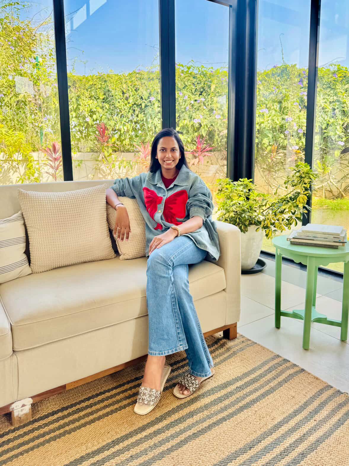Woman sitting on a beige sofa in a room with large windows and greenery outside