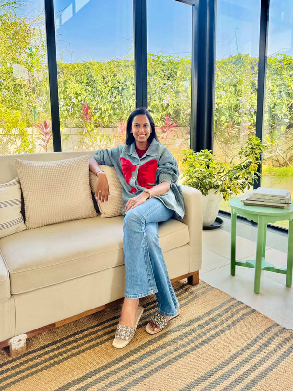 Woman sitting on a beige sofa in a room with large windows and greenery outside