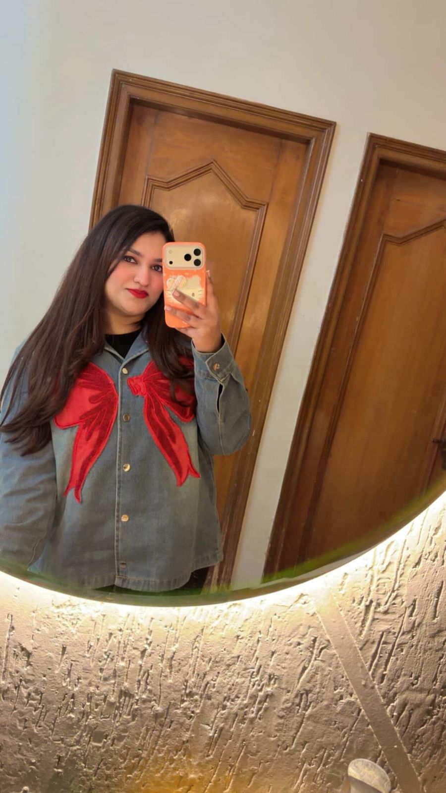 Person wearing a gray jacket with a red bow tie in front of a wooden door.
