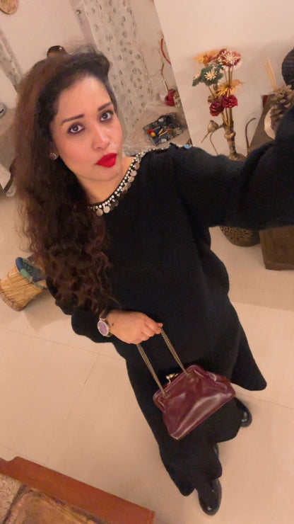 Woman in a black outfit holding a maroon handbag indoors.