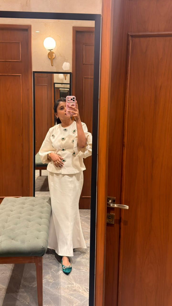 Person taking a mirror selfie wearing a white outfit in a room with wooden doors and a bench.