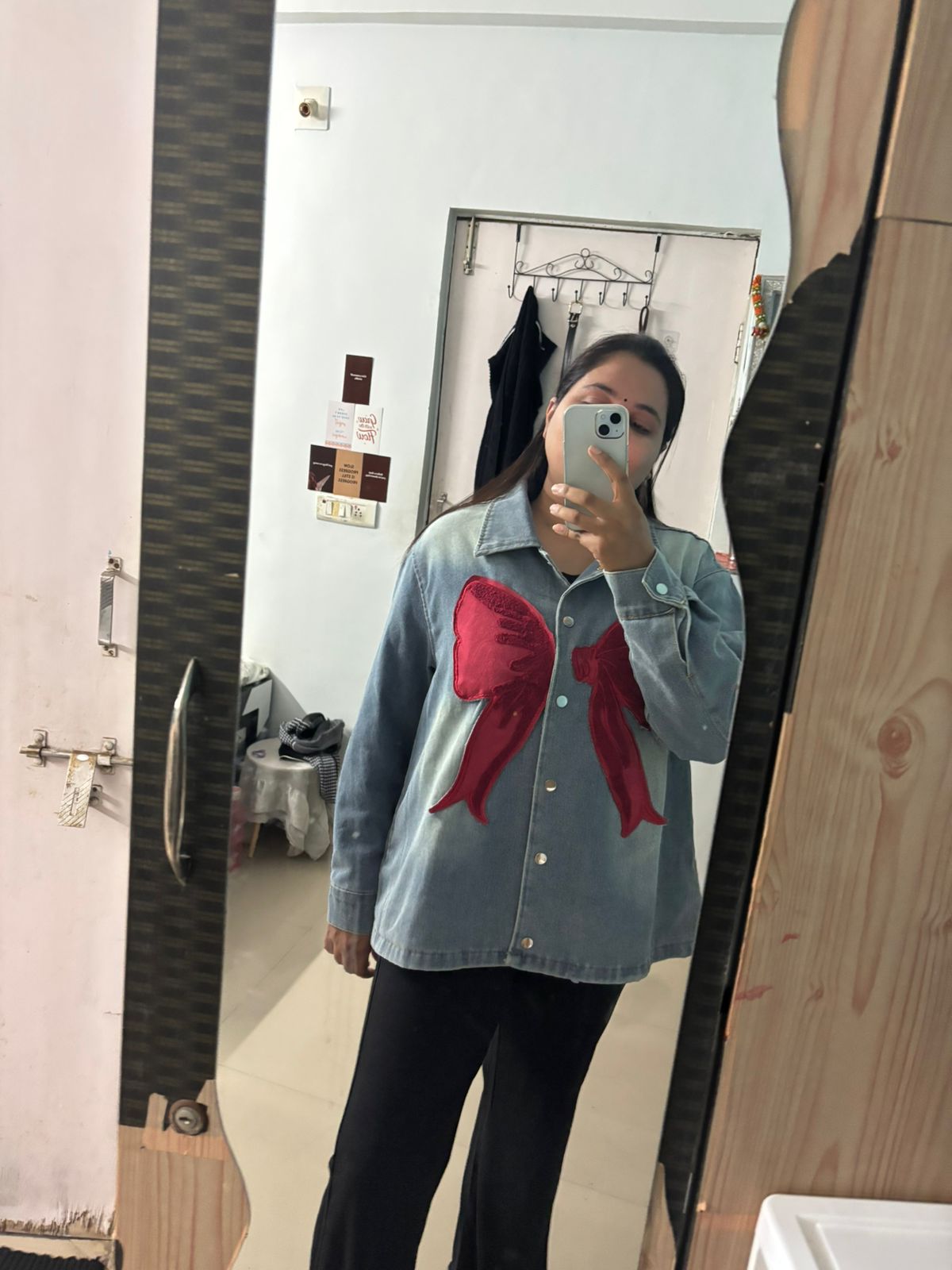 Person wearing a denim shirt with a red bow design in front of a mirror.