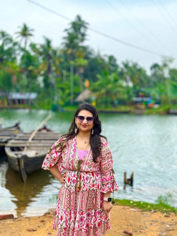 Woman in a pink dress standing by a river with boats and greenery in the background