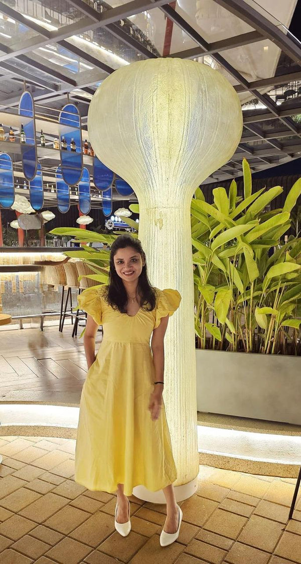 Woman in a yellow dress standing next to a large decorative light fixture in an indoor setting.