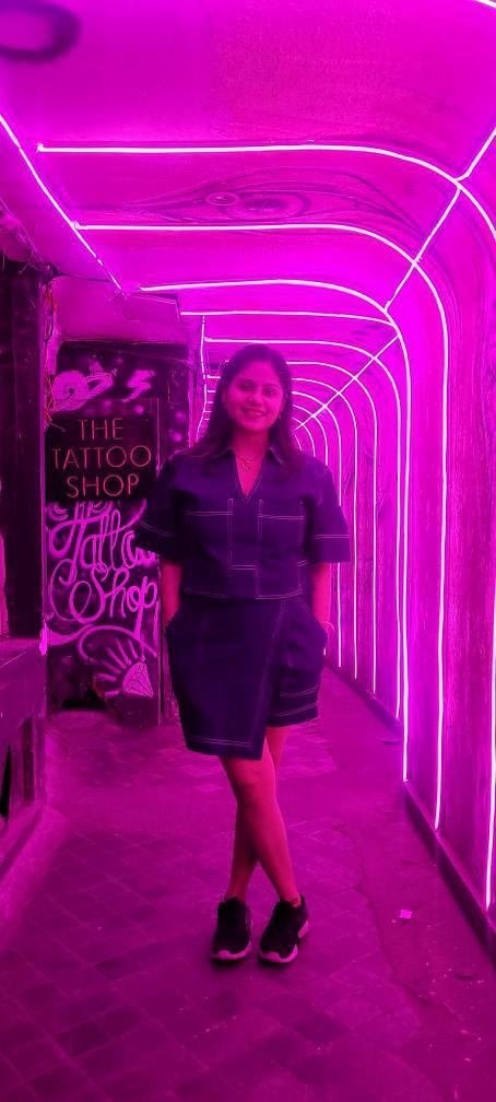 Person standing in a tunnel with pink neon lights, with 'The Tattoo Shop' sign on the left.