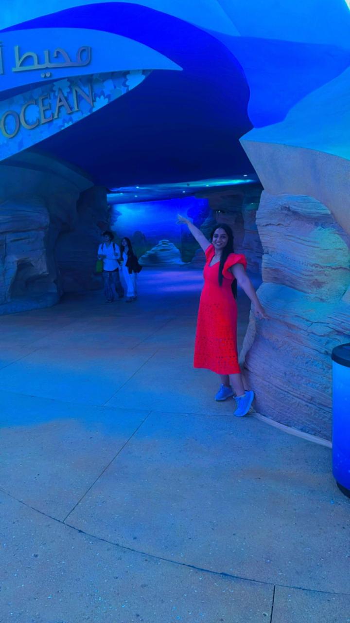 Woman in a red dress standing inside a blue-lit tunnel with 'OCEAN' text on a wall.